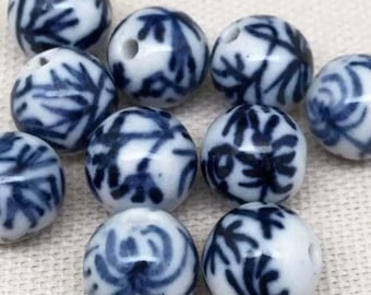 Peut inclure: Gros plan sur des perles blanches rondes ornées de motifs floraux bleus. Chaque perle est percée d'un trou. Les perles sont disposées sur une surface claire, mettant en valeur leur motif détaillé et leur potentiel créatif.