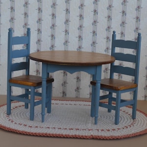 May include: A blue wooden table with a round top and two matching chairs. The table and chairs are set on a white crocheted oval rug.