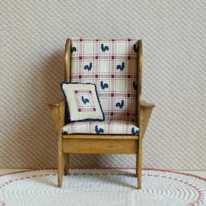May include: A miniature wooden armchair with a high back and rooster-patterned fabric. The chair has a small pillow with a matching rooster design. The fabric features a cream background with red plaid and navy blue rooster silhouettes.