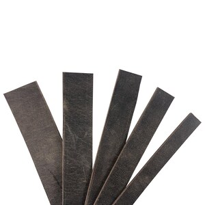 May include: A collection of five dark gray leather strips, each rectangular and varying slightly in width and length. The leather has a distressed, textured appearance, with visible grain and subtle color variations. The strips are arranged against a white background.