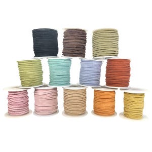 May include: A collection of spools of suede cord in various colors, including black, brown, green, blue, and orange. The cords are neatly wound on white spools, showcasing a range of hues suitable for crafting and jewelry making.