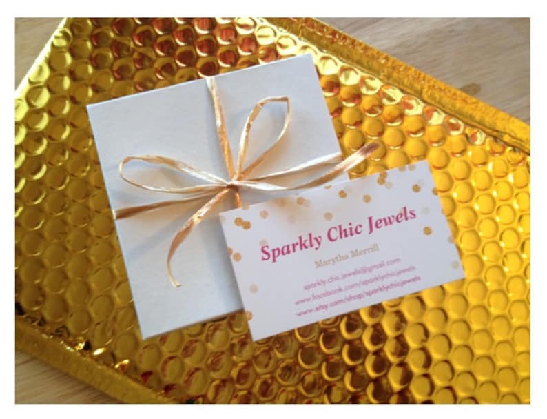 Pu&ograve; includere: Una scatola bianca con un nastro dorato legato intorno. La scatola &egrave; appoggiata su una busta di bolle dorata. Un biglietto da visita con il testo "Sparkly Chic Jewels" e il nome "Marytha Merrill" &egrave; visibile nell'immagine. Il biglietto da visita include anche l'indirizzo del sito web "sparklychicjewels@gmail.com", la pagina Facebook "www.facebook.com/sparklychicjewels" e il negozio Etsy "www.etsy.com/shop/sparklychicjewels".
