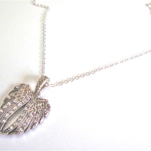 Puede incluir: Un collar de cadena de plata con un colgante con un par de alas de &aacute;ngel con diamantes de imitaci&oacute;n transparentes.