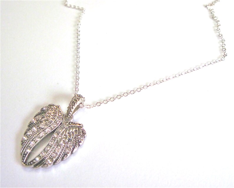 Puede incluir: Un collar de cadena de plata con un colgante con un par de alas de &aacute;ngel con diamantes de imitaci&oacute;n transparentes.