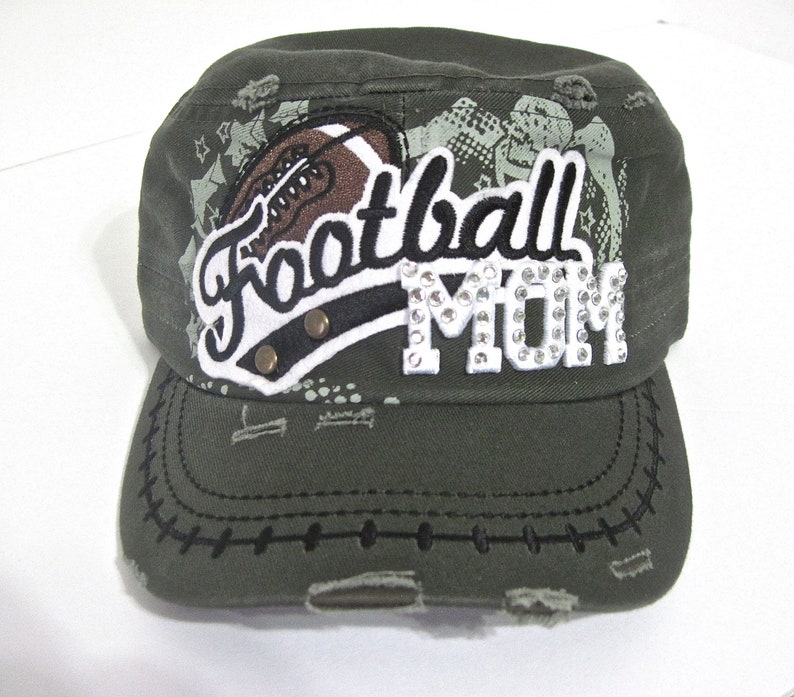 May include: A green camouflage baseball cap with a distressed look. The cap has a white patch with the words "Football Mom" in black lettering and rhinestones. A brown football graphic is on the patch.