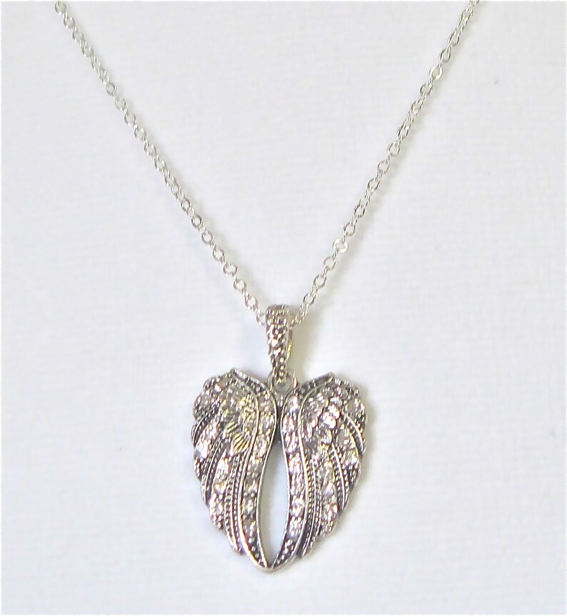 Puede incluir: Un collar de plata con un colgante en forma de coraz&oacute;n que presenta dos alas de &aacute;ngel adornadas con brillantes diamantes de imitaci&oacute;n.