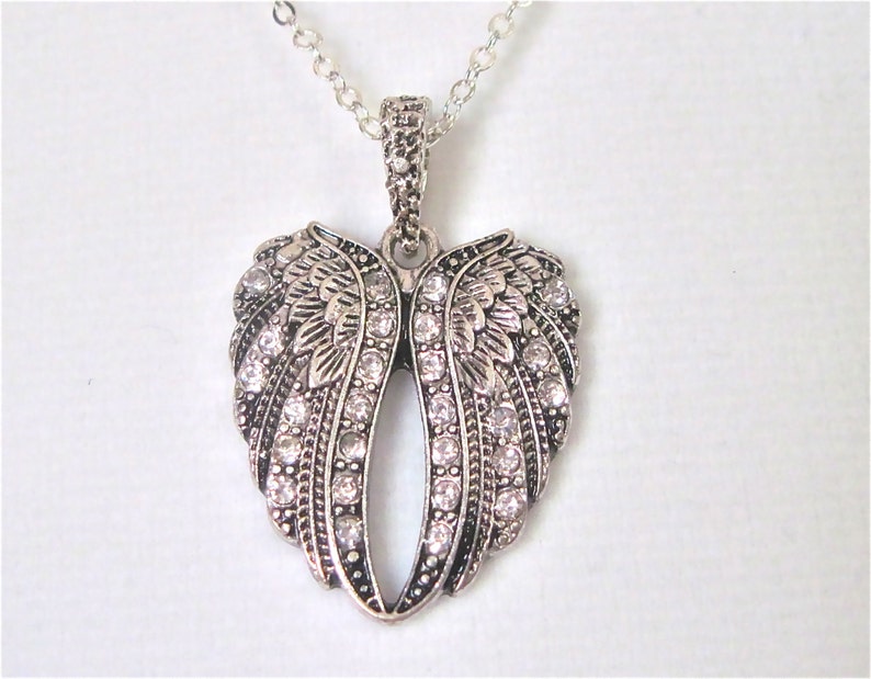 Puede incluir: Collar plateado con un colgante en forma de coraz&oacute;n con alas de &aacute;ngel adornadas con brillantes transparentes.