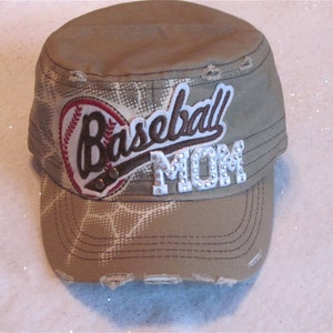 May include: A tan baseball cap with a white and brown baseball graphic and the text "Baseball Mom" in white with rhinestones.