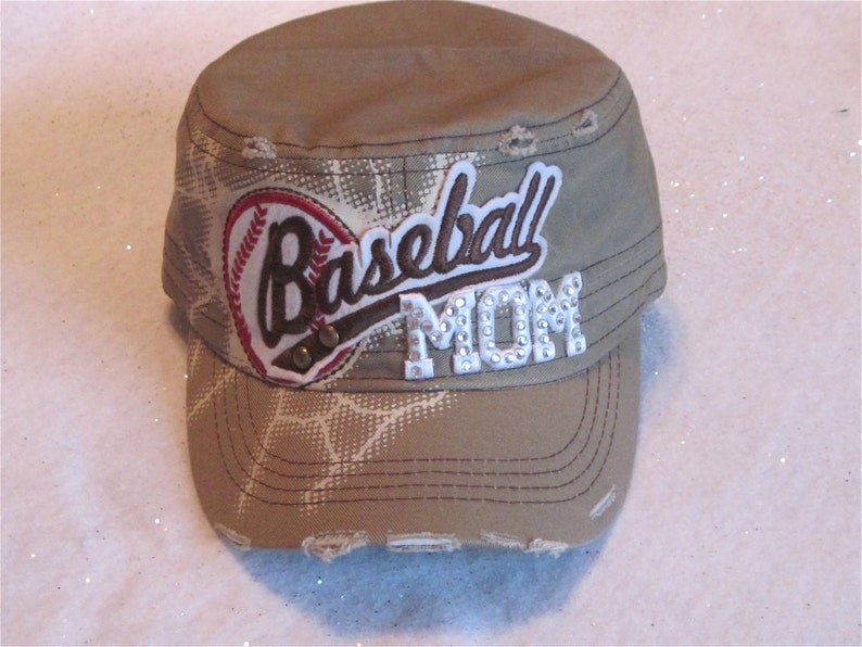 May include: A tan baseball cap with a white and brown baseball graphic and the text "Baseball Mom" in white with rhinestones.
