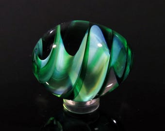 May include: A green and white glass marble with swirling patterns. The marble is round and has a glossy finish.