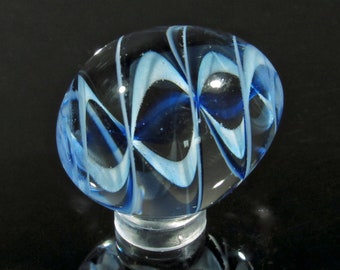 May include: A blue and white glass marble with a swirling pattern. The marble is on a clear stand.
