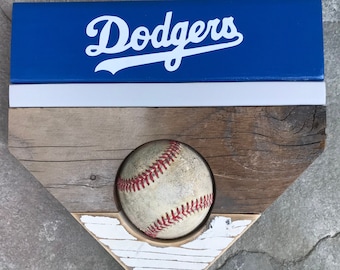 May include: A wooden home plate with a white and blue sign that says "Dodgers" and a baseball in the center.