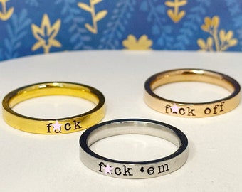 May include: Three gold, rose gold, and silver rings with the words "f*ck", "f*ck off", and "f*ck 'em" engraved on them.