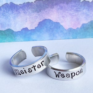 May include: Two silver rings with the words "Meister" and "Weapon" engraved on them.
