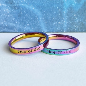 May include: Two iridescent rainbow colored metal rings with the words "ride or die" engraved on them.