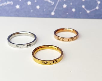 May include: Three simple silver, gold, and rose gold rings with the phrase "Bad Bitch" engraved on each.