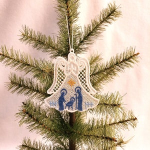 May include: White lace Christmas ornament with a blue nativity scene inside. The ornament is shaped like an angel with a star on top.