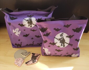 May include: Two purple Halloween tote bags with black bats, ghosts, and witches flying on a white moon. The bags have black handles and are made of canvas. There are four wooden Halloween stamps on a wooden surface.