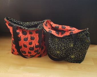 May include: Two tote bags, one with a black cat pattern on an orange background and the other with a black and green spiderweb pattern.