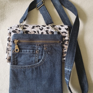 May include: A denim crossbody bag with a zipper closure and a front pocket. The bag has a leopard print fabric lining and a denim strap.