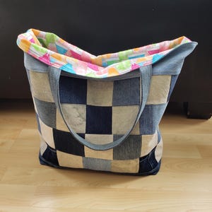 May include: A patchwork tote bag with a checkerboard pattern in various shades of denim. The bag has a colourful patterned lining and denim handles. The bag is open, revealing the interior lining.