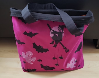 May include: A pink tote bag with black handles and a Halloween theme. The bag is decorated with bats, ghosts, spiders, and a witch flying on a broomstick.