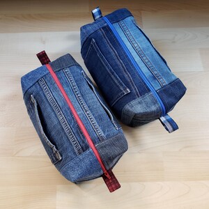 Peut inclure: Deux trousses en jean avec des fermetures éclair de couleurs contrastées. L'une a une fermeture éclair rouge, l'autre une fermeture éclair bleue. Les deux ont une forme rectangulaire, des poignées et sont fabriquées à partir de denim recyclé.