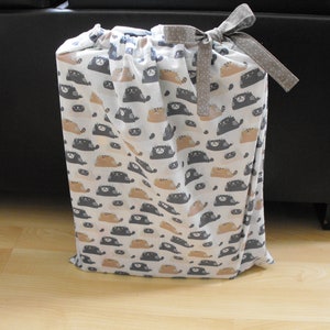 May include: A white drawstring bag with a black and brown cat print. The bag has a gray and white polka dot ribbon tied around the top.