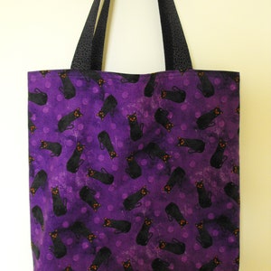 Peut inclure: Sac fourre-tout violet avec un imprimé de chat noir et des pois noirs. Le sac a des anses noires.