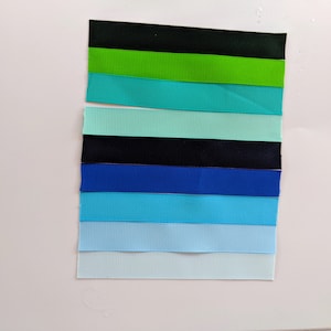 May include: A collection of eight ribbon samples in various shades of blue, green, and black. The ribbons are arranged vertically in a row, with the darkest color at the top and the lightest color at the bottom.
