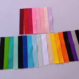 May include: Assortment of 20 different colored ribbon spools. The ribbons are all the same width and are arranged in two rows. The top row has 8 ribbons in shades of red, pink, and purple. The bottom row has 12 ribbons in shades of green, blue, black, white, yellow, and orange.