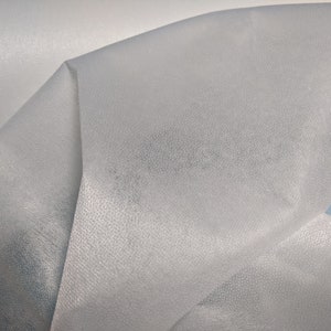 May include: Close-up of a white, sheer fabric with a textured surface. The fabric is folded and draped, creating soft folds and curves.