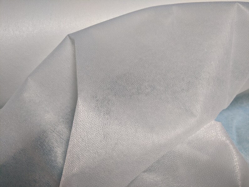 May include: Close-up of a white, sheer fabric with a textured surface. The fabric is folded and draped, creating soft folds and curves.