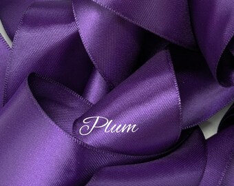 May include: Close-up of plum-colored satin ribbon. The ribbon is tightly curled and layered, creating a textured effect. The word "Plum" is written in a cursive font on the ribbon. This ribbon is suitable for crafts, gift wrapping, and decorative purposes.