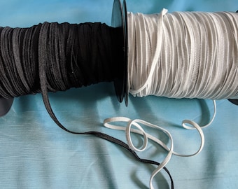 Pode incluir: Dois rolos de cordão elástico, um preto e outro branco, estão enrolados em torno de rolos de plástico preto. Os rolos estão sobre uma superfície azul.
