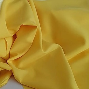 May include: A bright yellow fabric with a smooth, silky texture. The fabric is folded and draped, showcasing its soft and flowing nature.
