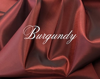 May include: A piece of burgundy fabric with a smooth, slightly iridescent finish and deep folds. The word Burgundy is written in a white, cursive script font across the center of the fabric, highlighting the rich, dark red color of the material.