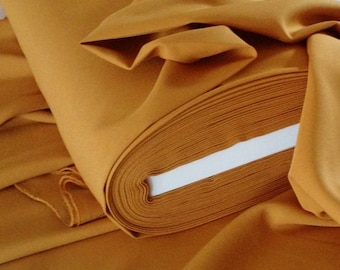 Pode incluir: Um rolo de tecido amarelo mostarda. O tecido está dobrado ao meio e o rolo é visível.