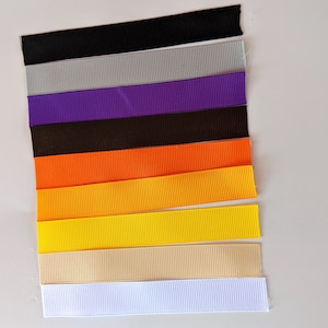 May include: Assortment of ten different colored ribbon spools. The colors are black, gray, purple, brown, orange, yellow, beige, and white.