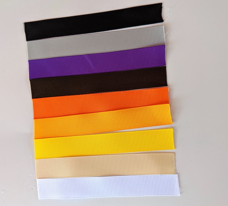 May include: Assortment of ten different colored ribbon spools. The colors are black, gray, purple, brown, orange, yellow, beige, and white.
