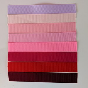 May include: A collection of eight different colored ribbon spools. The colors range from light purple to dark burgundy. The ribbon is a satin material with a slight sheen.