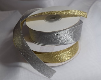 May include: Two spools of ribbon, one silver and one gold, with a glittery finish. The ribbon is wrapped around cardboard spools.