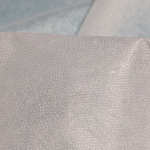 May include: Close-up of a white, textured fabric with a fine, dotted pattern. The fabric has a slightly translucent quality.