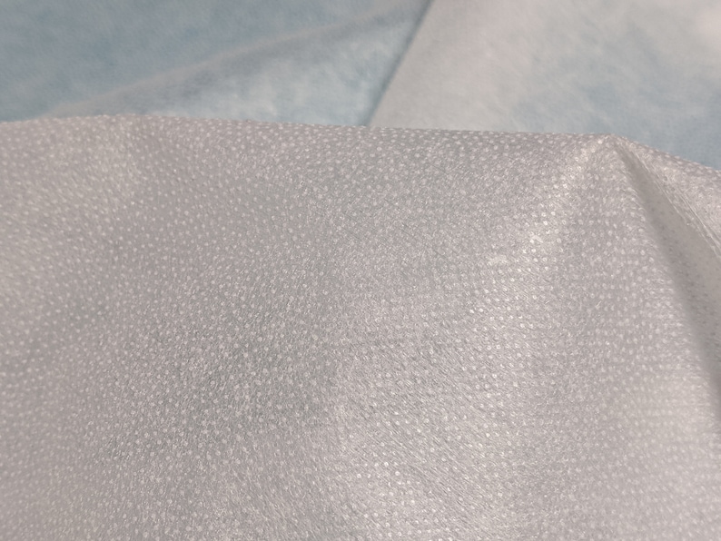 May include: Close-up of a white, textured fabric with a fine, dotted pattern. The fabric has a slightly translucent quality.