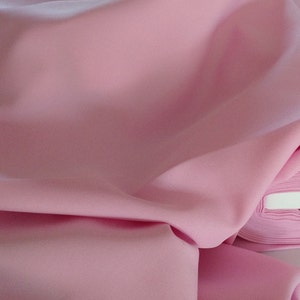 May include: A close-up of a soft, pink fabric folded in a smooth, flowing drape. The fabric is smooth and has a subtle sheen.