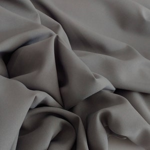 May include: A close-up of a gray fabric with soft folds and wrinkles. The fabric has a smooth, even texture.