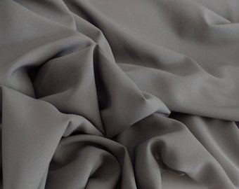 May include: A close-up of a gray fabric with soft folds and wrinkles. The fabric has a smooth, even texture.