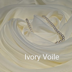 May include: Ivory voile fabric with a strand of white pearls draped on top. The fabric is gathered and folded to create a soft, flowing look.  Ivory Voile.
