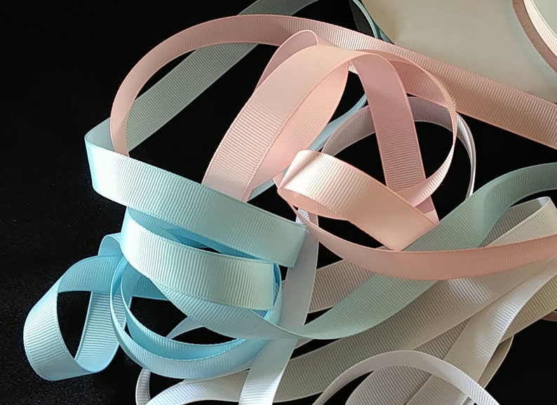 May include: A collection of pastel colored ribbon in pink, light blue, and white. The ribbon is woven with a textured pattern.