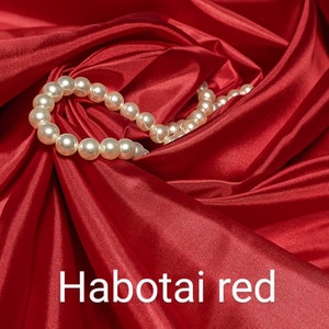 May include: A close-up of a smooth, red fabric with a strand of white pearls draped across it. The fabric is called "Habotai red".